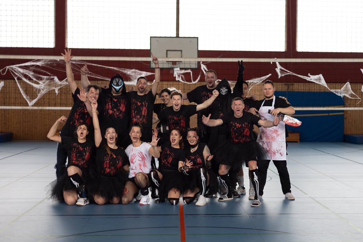 Teamfoto in Halloween-Kostümen vor dem dekorierten Netz